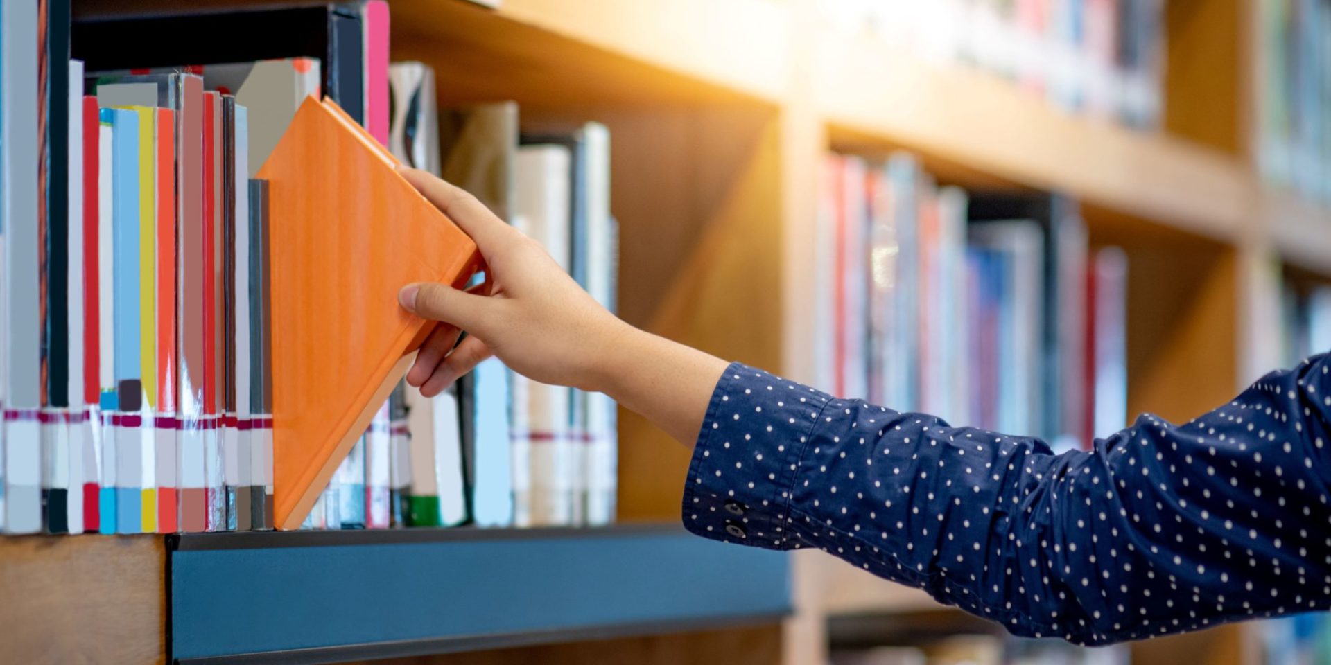 Woman in blue shirt grabs orange book from library shelf.