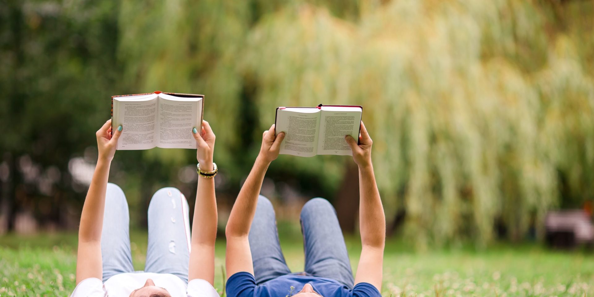 A couple laying down reading books in a peaceful field.