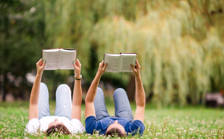 A couple laying down reading books in a peaceful field.
