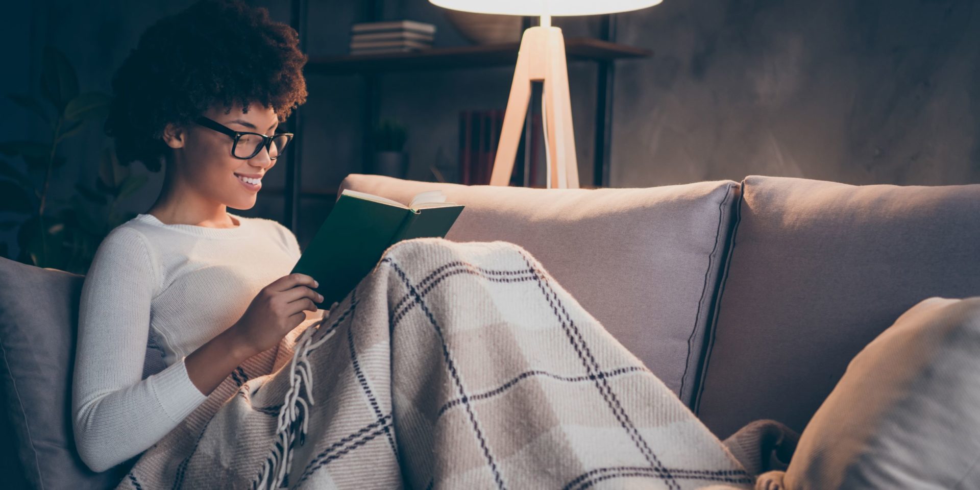 Woman wearing glasses reading a poetry book on a couch at night.