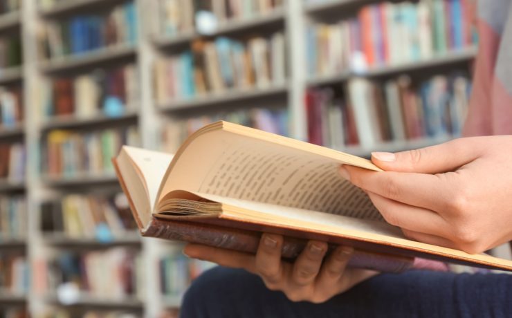 Person reading an old physical book in a library.