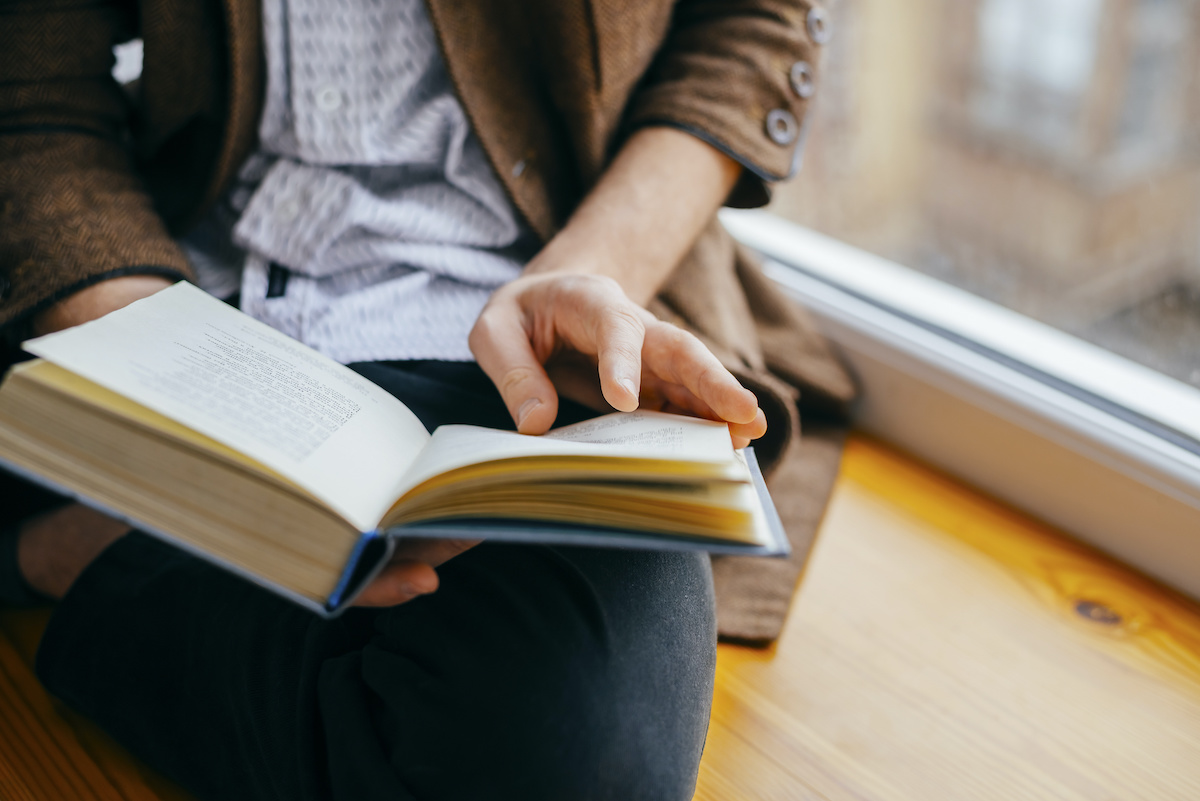 Young man reading a military history book next to a windowsill.