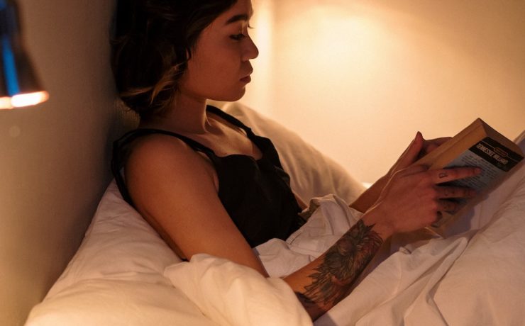Woman reading a book in bed to reduce stress and anxiety.